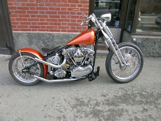 An orange motorcycle with a custom round oil tank featuring a spade and the number 13 cut into the metal.